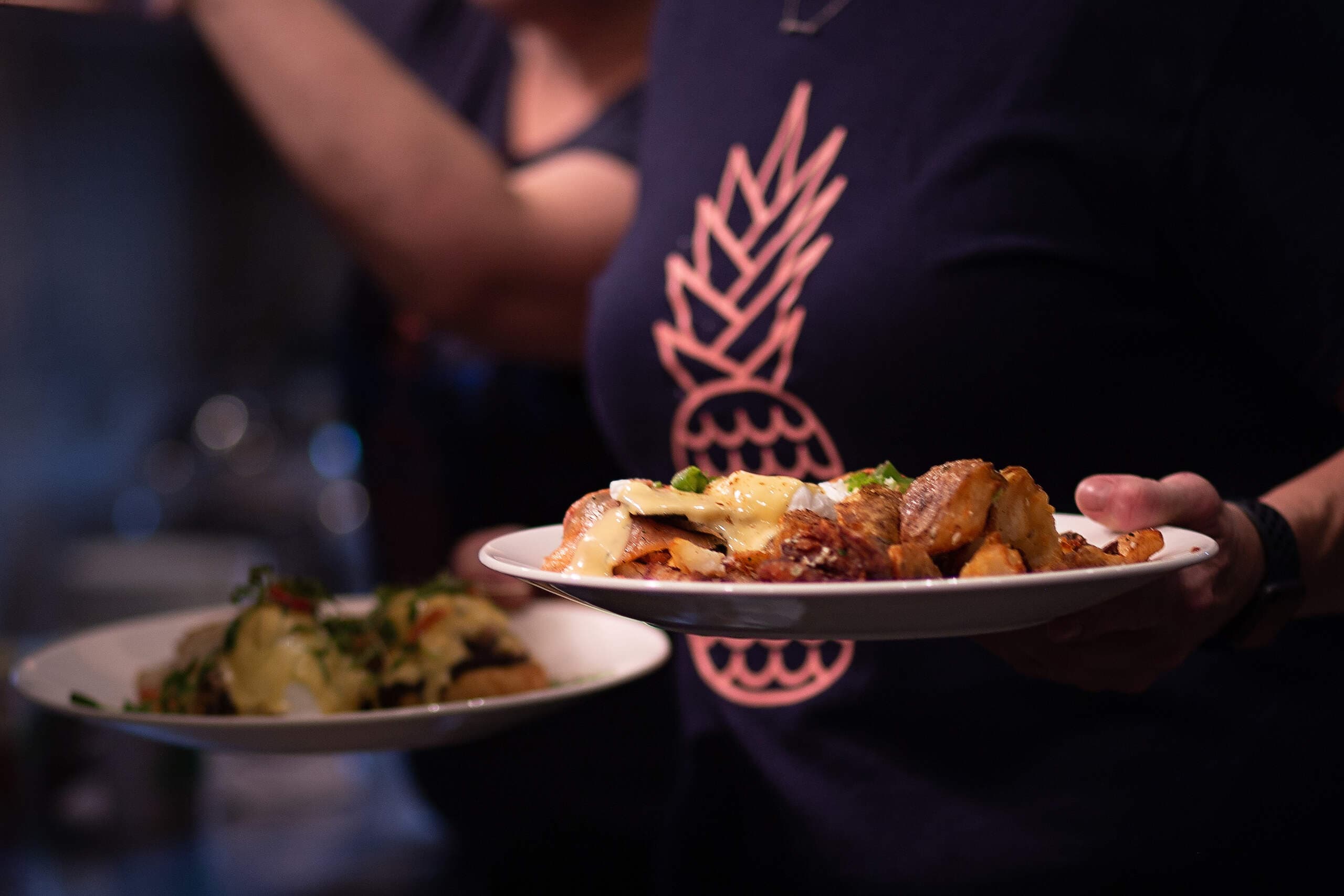 Server carrying two plates of eggs benedict and breakfast hash at Benedicts
