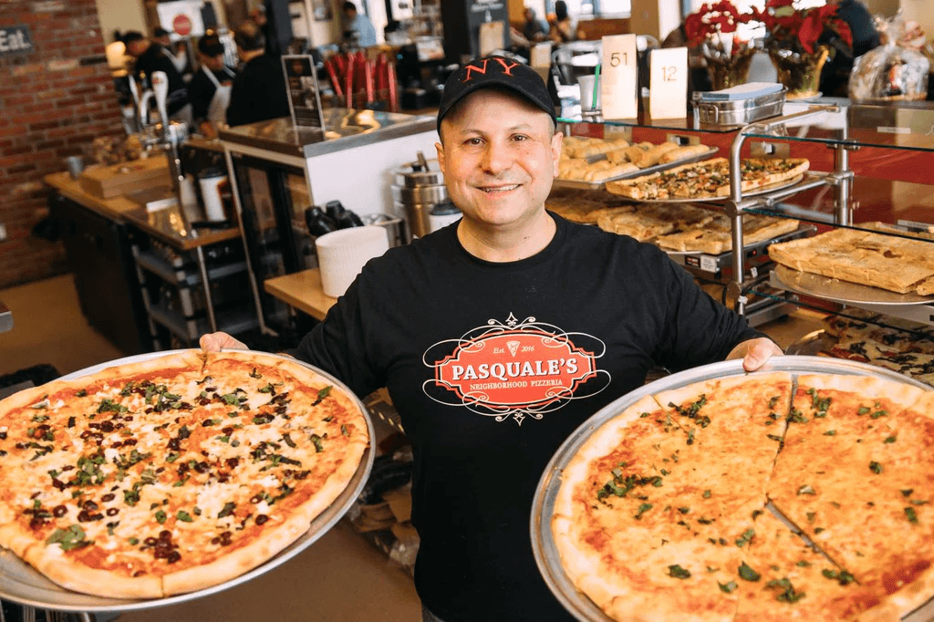 Pasquale's pizzaiolo holding two New York style pizzas