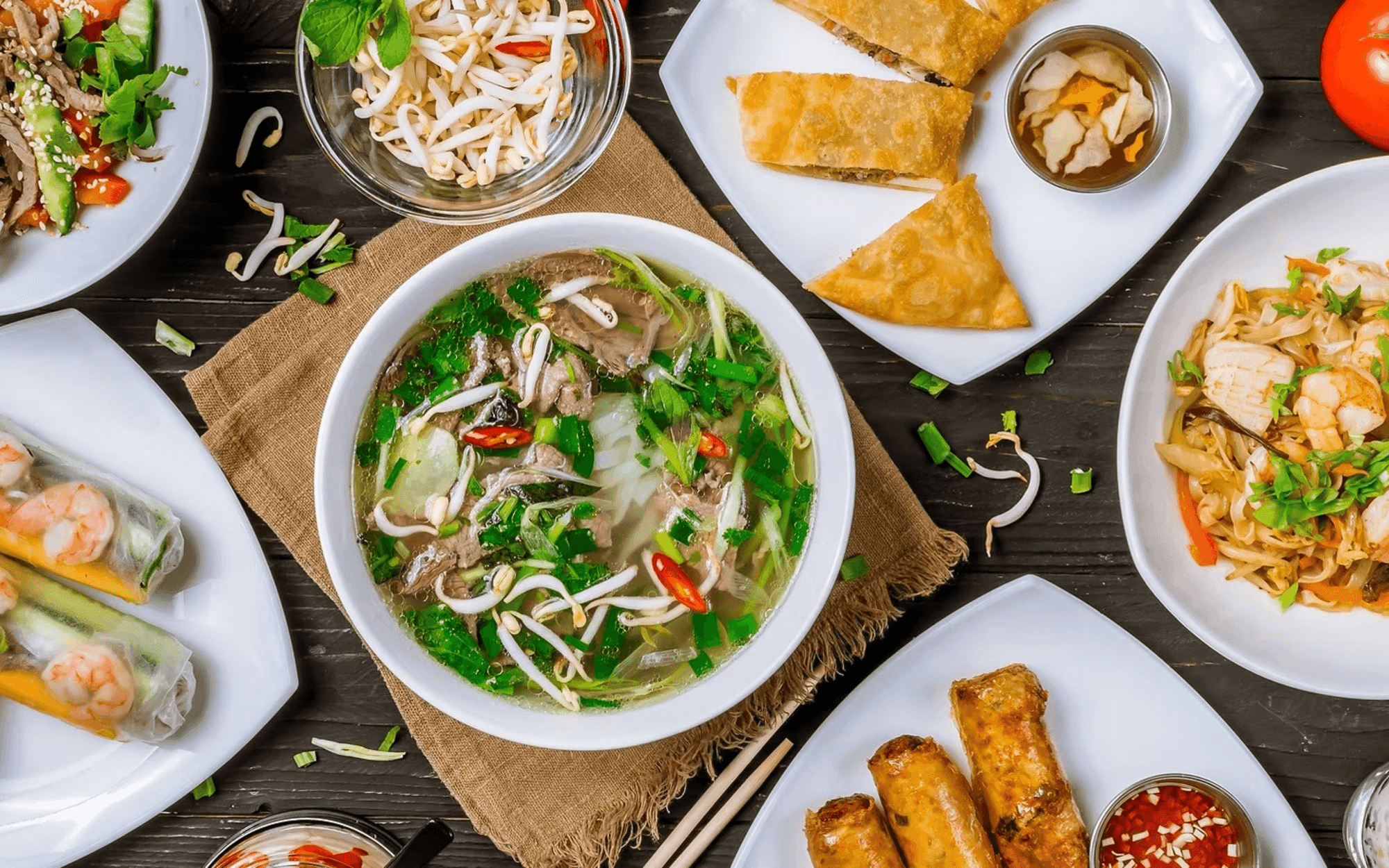 Spread of Vietnamese dishes including a bowl of pho, spring rolls, and egg rolls at Pho Chau